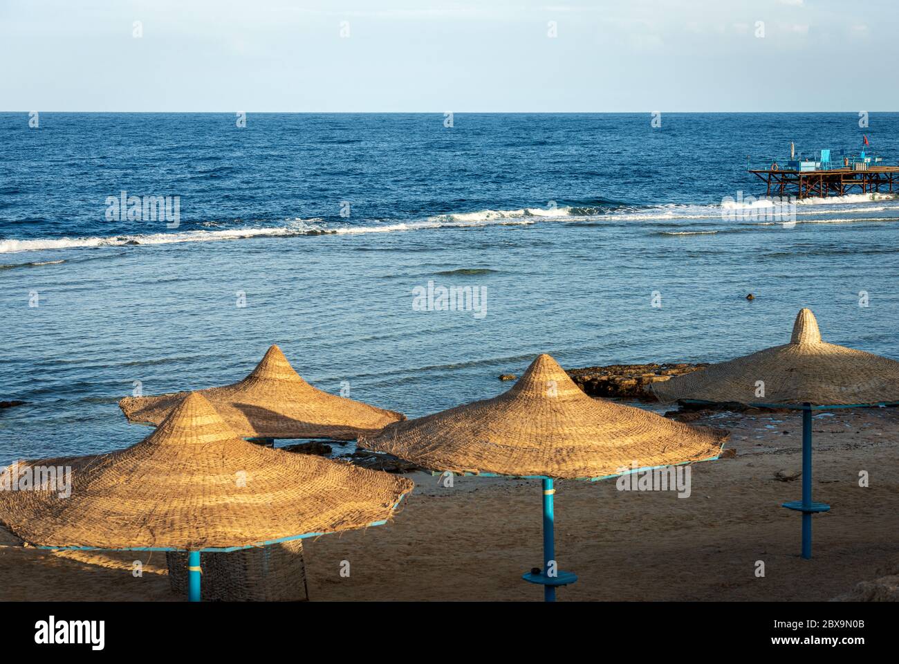 Stroh Strandschirme und Seenlandschaft in der Nähe von Marsa Alam, Rotes Meer, Ägypten, Afrika. Die Wellen des Meeres stürzen auf dem Korallenriff. Stockfoto