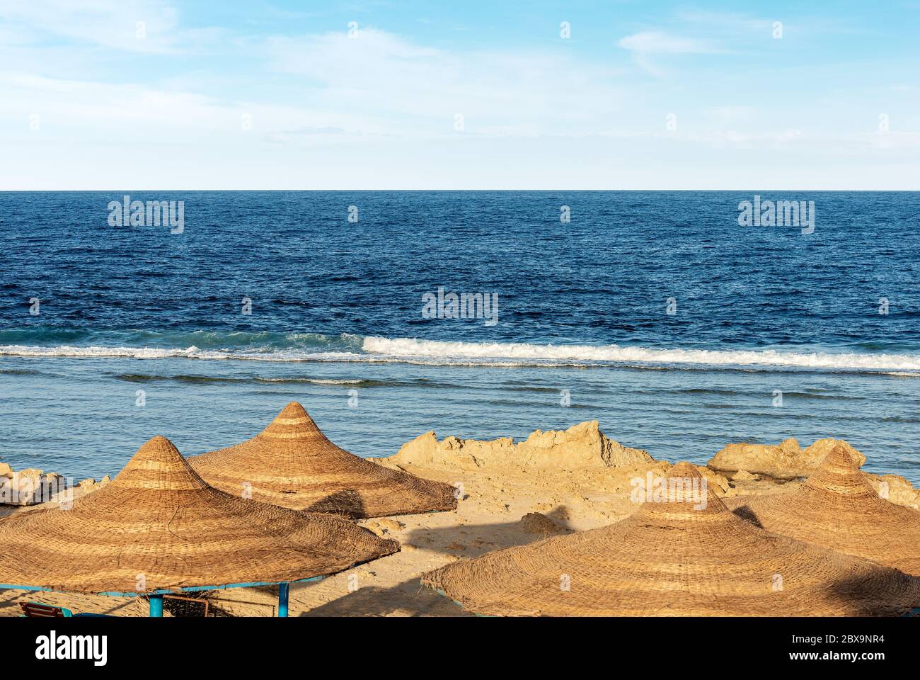 Strand am Roten Meer mit Strohschirmen in der Nähe von Marsa Alam, Ägypten, Afrika. Die Wellen des Meeres stürzen auf dem Korallenriff Stockfoto