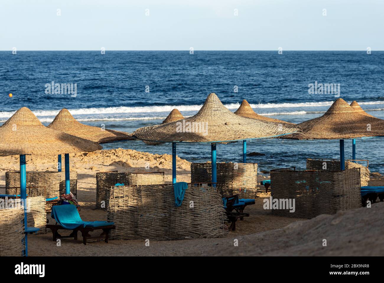 Strand am Roten Meer mit Strohschirmen und Liegestühlen in der Nähe von Marsa Alam, Ägypten, Afrika. Die Wellen des Meeres stürzen auf dem Korallenriff Stockfoto