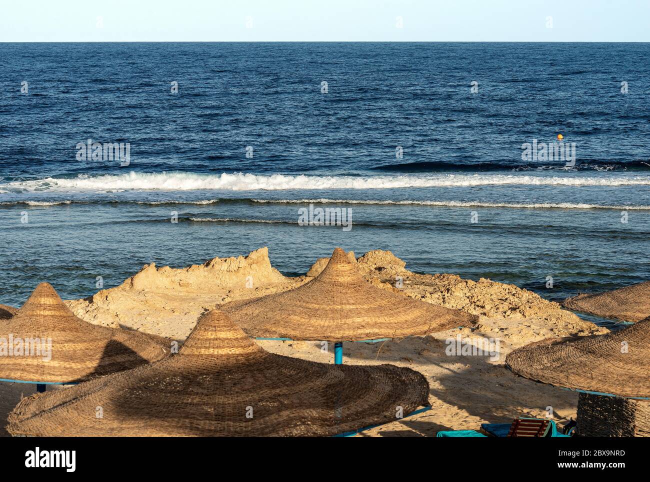 Strand am Roten Meer mit Strohschirmen in der Nähe von Marsa Alam, Ägypten, Afrika. Die Wellen des Meeres stürzen auf dem Korallenriff Stockfoto