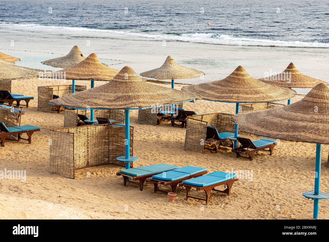 Strand am Roten Meer mit Strohschirmen und Liegestühlen in der Nähe von Marsa Alam, Ägypten, Afrika. Die Wellen des Meeres stürzen auf dem Korallenriff Stockfoto