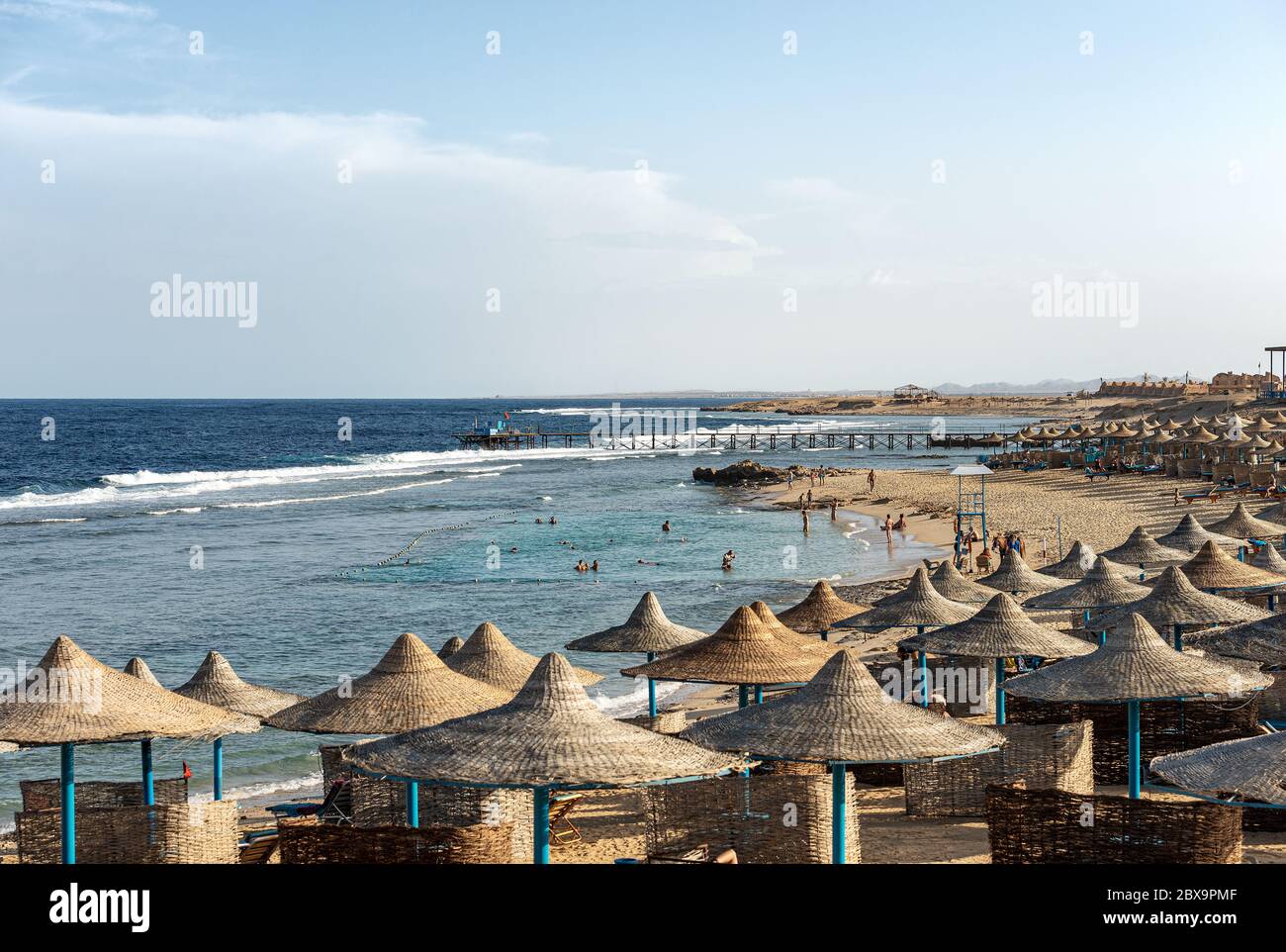 Sandstrand mit vielen Strohschirmen und Liegestühlen in der Nähe von Marsa Alam, Rotes Meer, Ägypten, Afrika.die Touristen sonnen, schwimmen oder schnorcheln Stockfoto