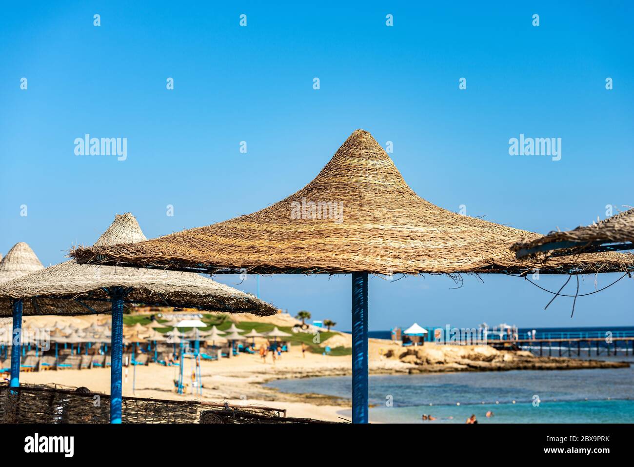 Gruppe von Strohschirmen in einem Roten Meer Strand auf einem klaren blauen Himmel, in der Nähe von Marsa Alam, Ägypten, Afrika. Stockfoto