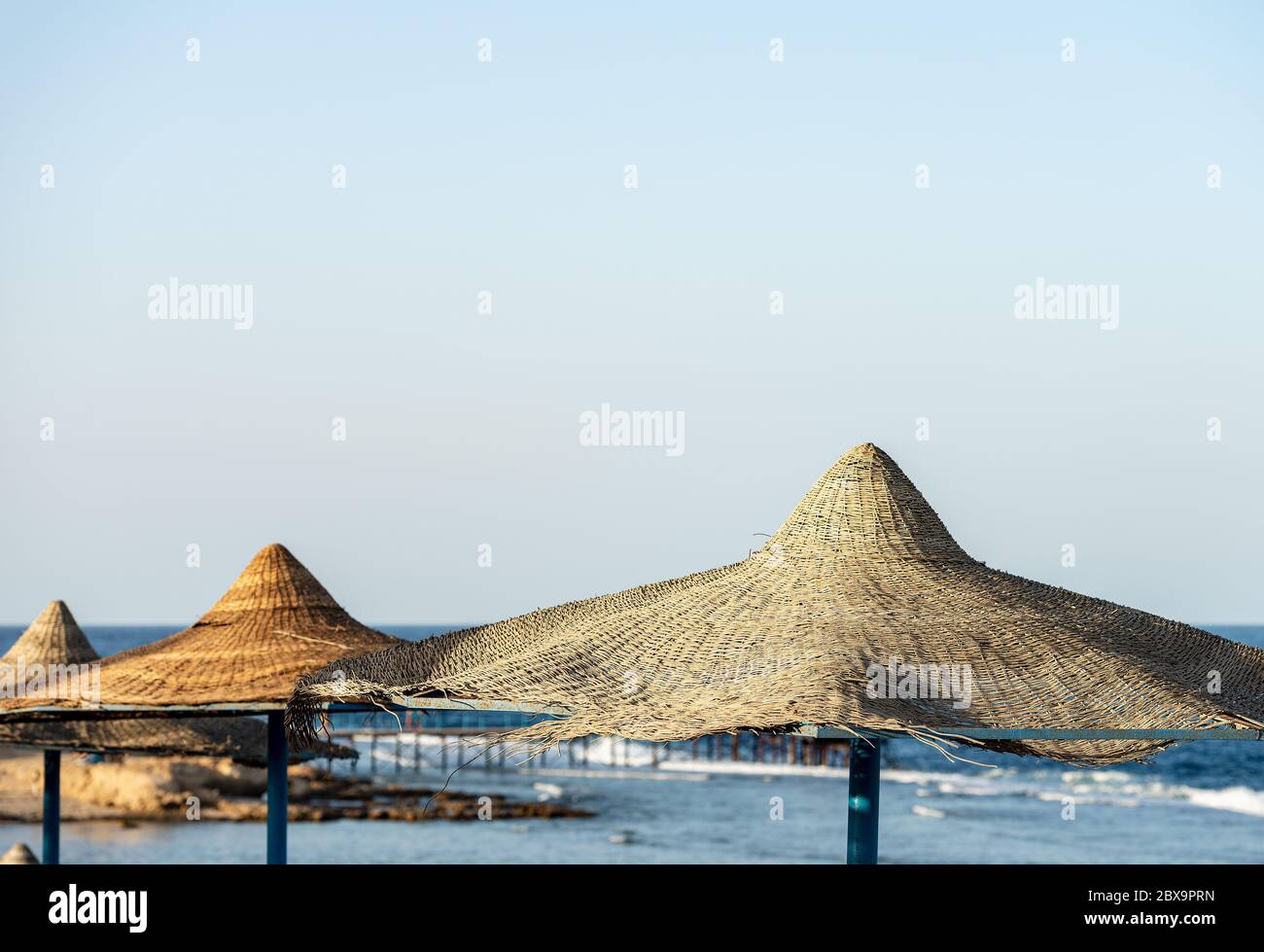 Strohschirme in einem Roten Meer Strand, in der Nähe von Marsa Alam, Ägypten, Afrika. Im Hintergrund das Meer mit den Wellen am Korallenriff Stockfoto