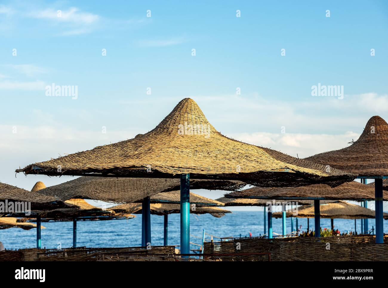 Stroh-Sonnenschirme mit dem Roten Meer und blauen Himmel mit Wolken auf dem Hintergrund. Marsa Alam, Ägypten, Afrika. Stockfoto