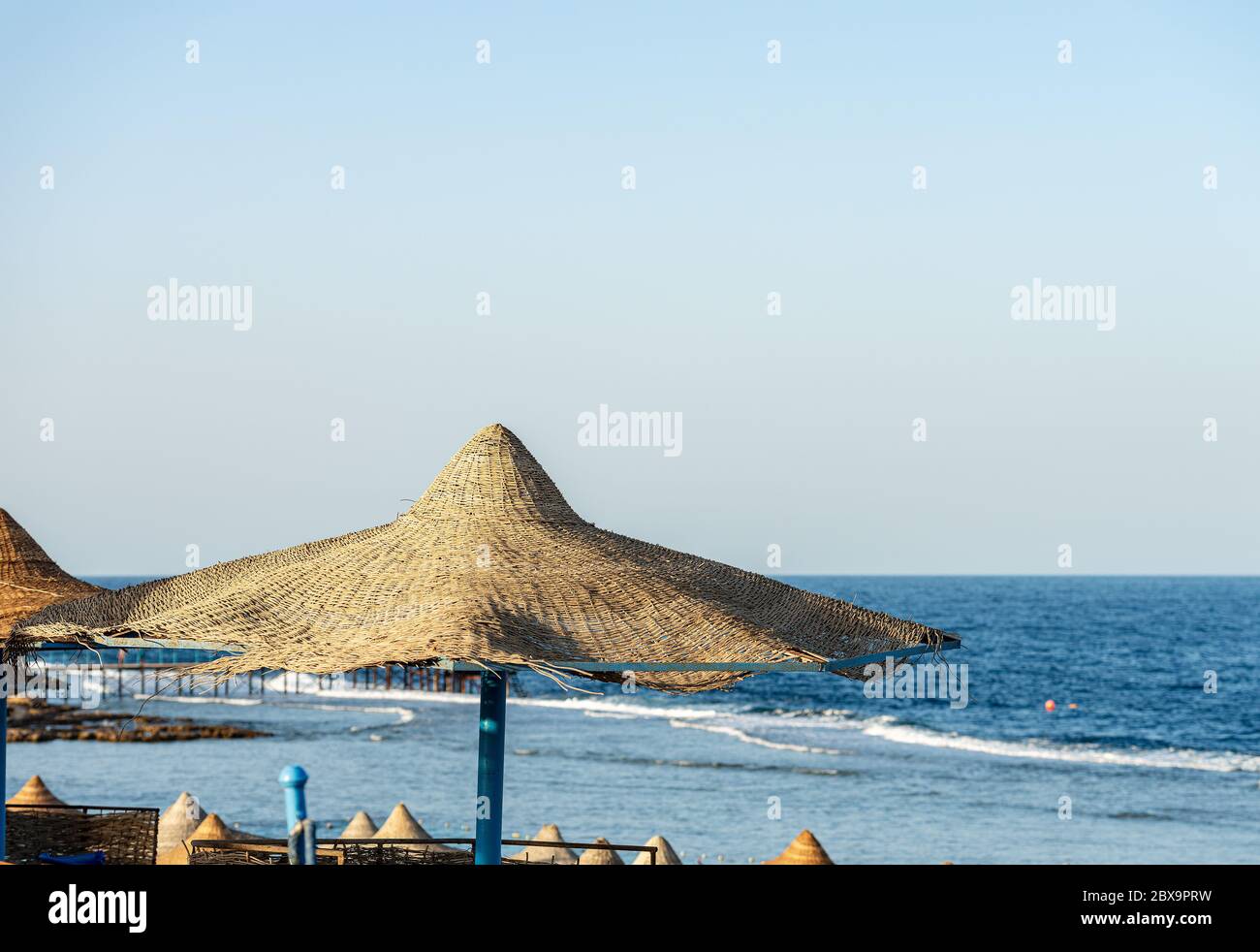 Strohschirme in einem Roten Meer Strand, in der Nähe von Marsa Alam, Ägypten, Afrika. Die Wellen des Meeres stürzen auf dem Korallenriff Stockfoto