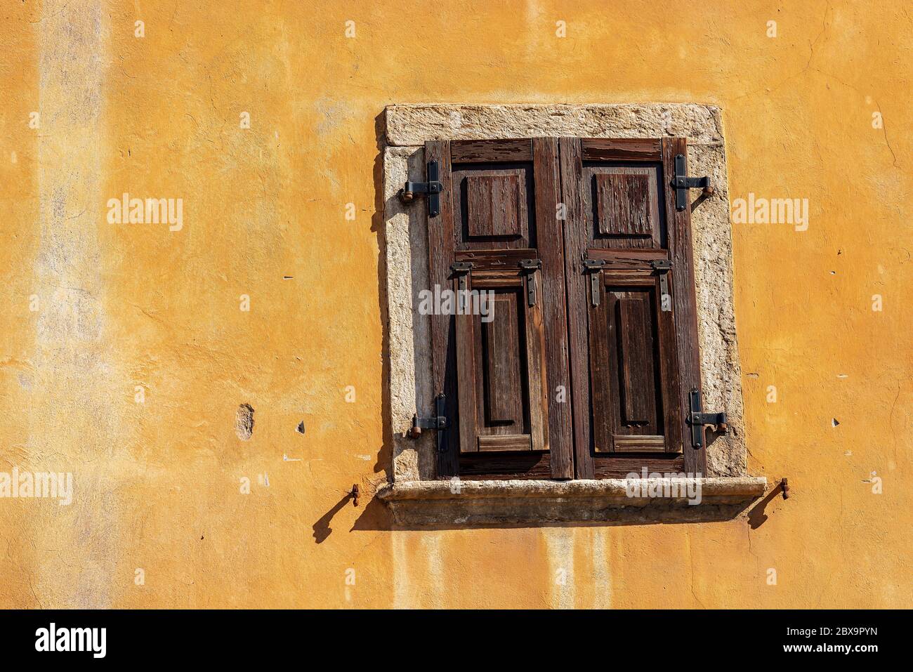 Nahaufnahme eines alten Fensters mit geschlossenen braunen Holzfensterläden an einer orangefarbenen Wand. Trentino-Südtirol, Italien, Europa Stockfoto