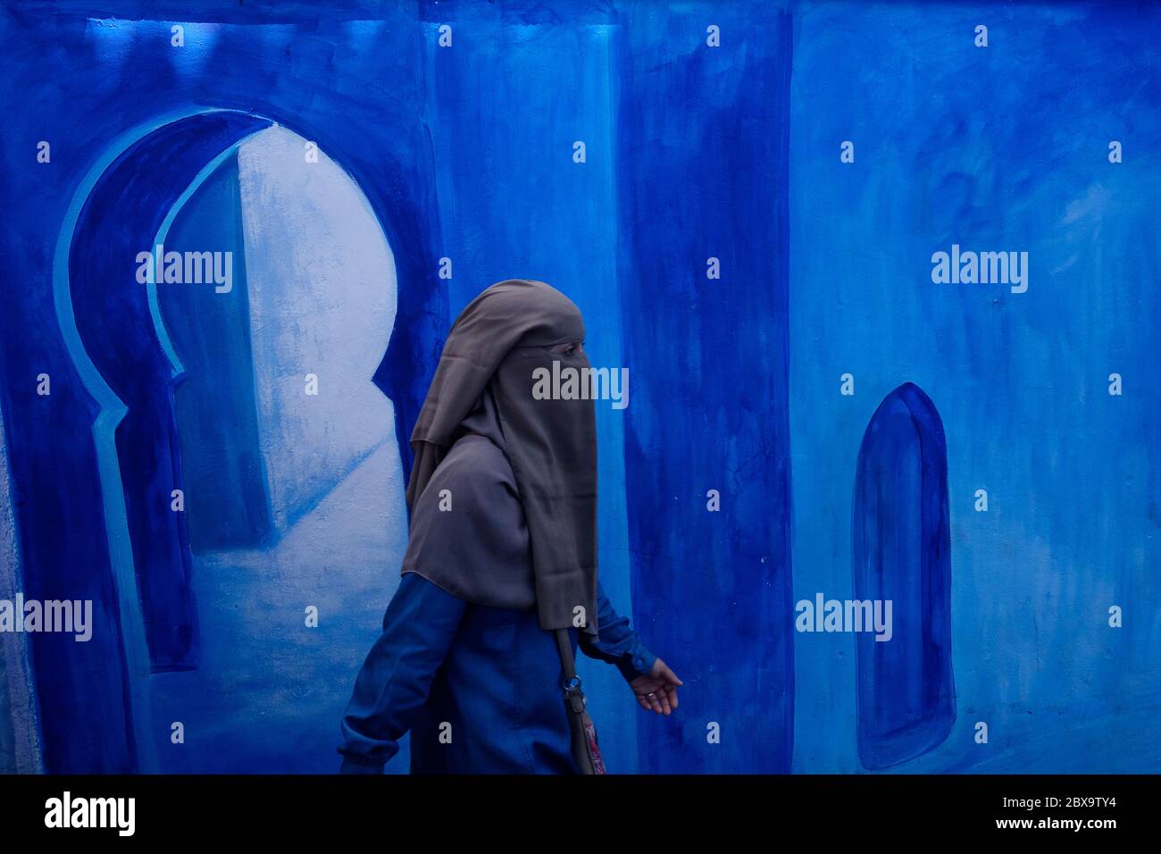 Eine Frau mit Niqab geht vor einem blau dekorierten Wandbild in der alten Medina. Chefchaouen. Djabala - Rif Region. Tanger - Provinz Tetuan. Norden Stockfoto