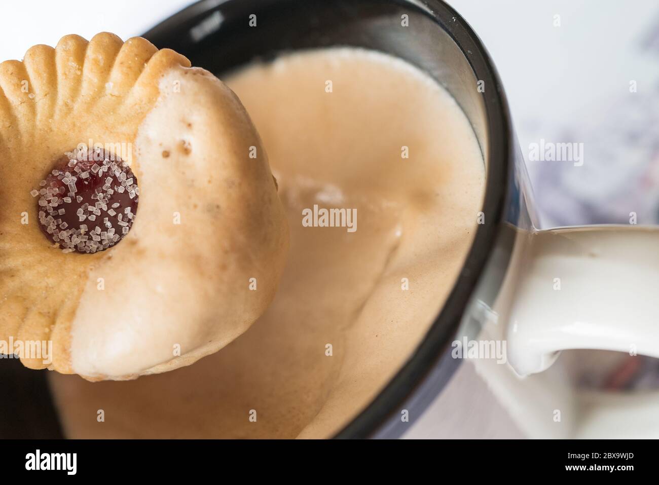 Gezuckerte Marmelade Ring Keks wird in schaumigen Kaffee in einem Becher getunked Stockfoto