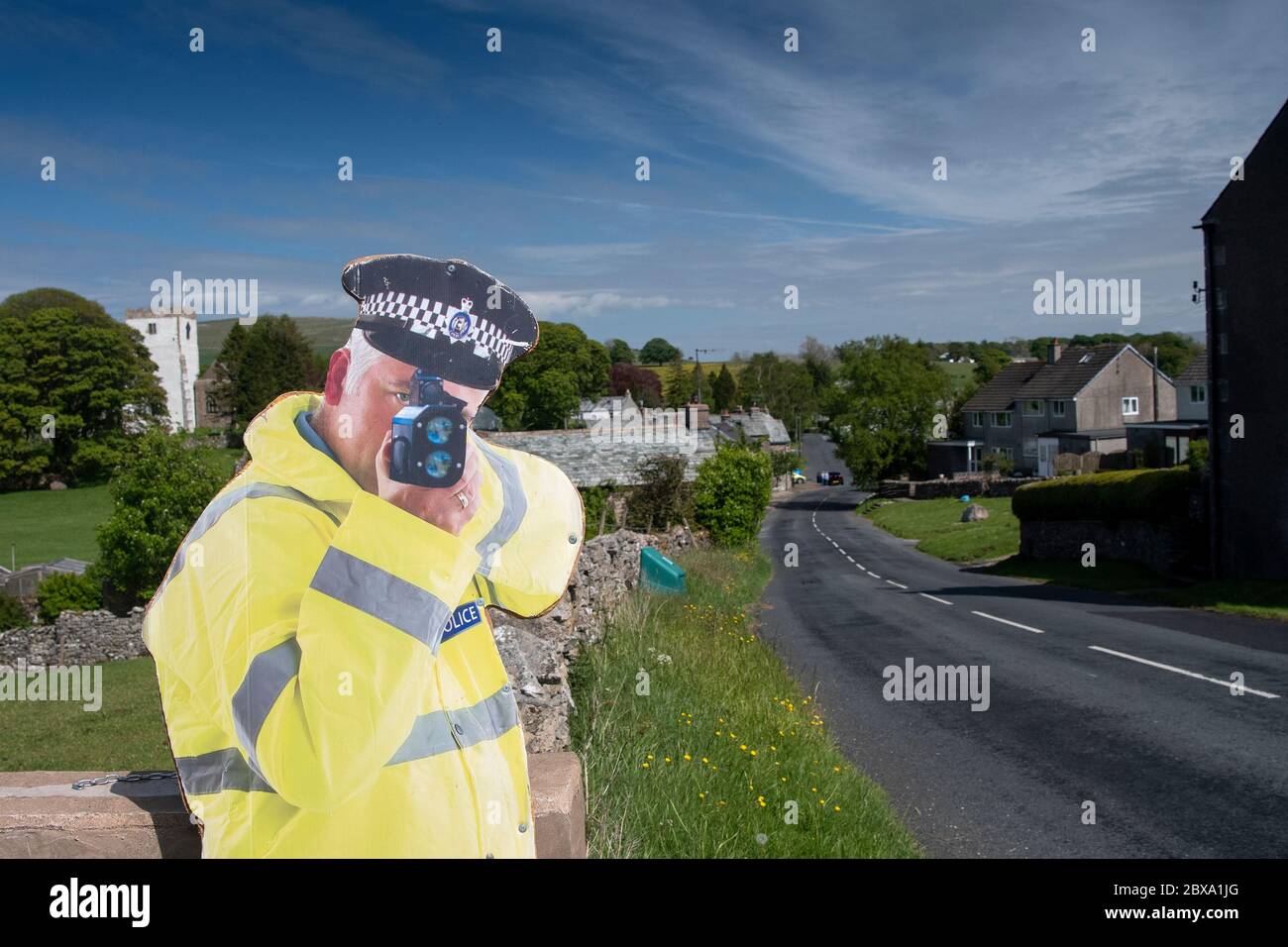 Karton Ausschnitt eines Polizisten mit einer Geschwindigkeitspistole, um den Verkehr auf dem Weg zu einem Dorf zu verlangsamen. Cumbria, Großbritannien. Stockfoto