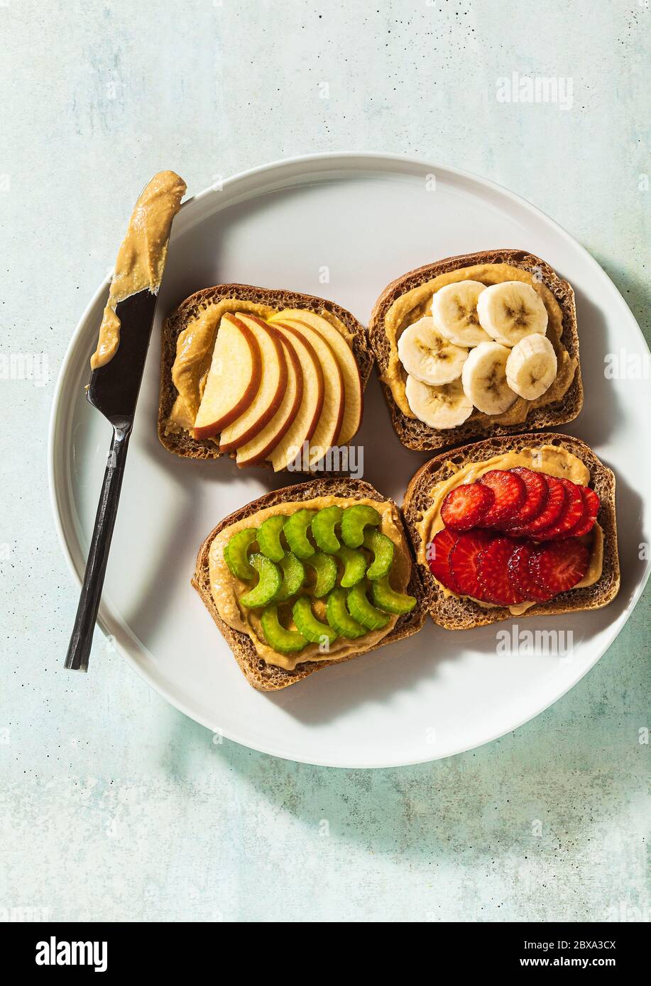 Verschiedene Sandwiches mit Erdnussbutter und Erdbeeren, Sellerie, Banane und Apfel auf einem Teller auf dem Tisch. Perfektes Frühstück am Morgen Stockfoto