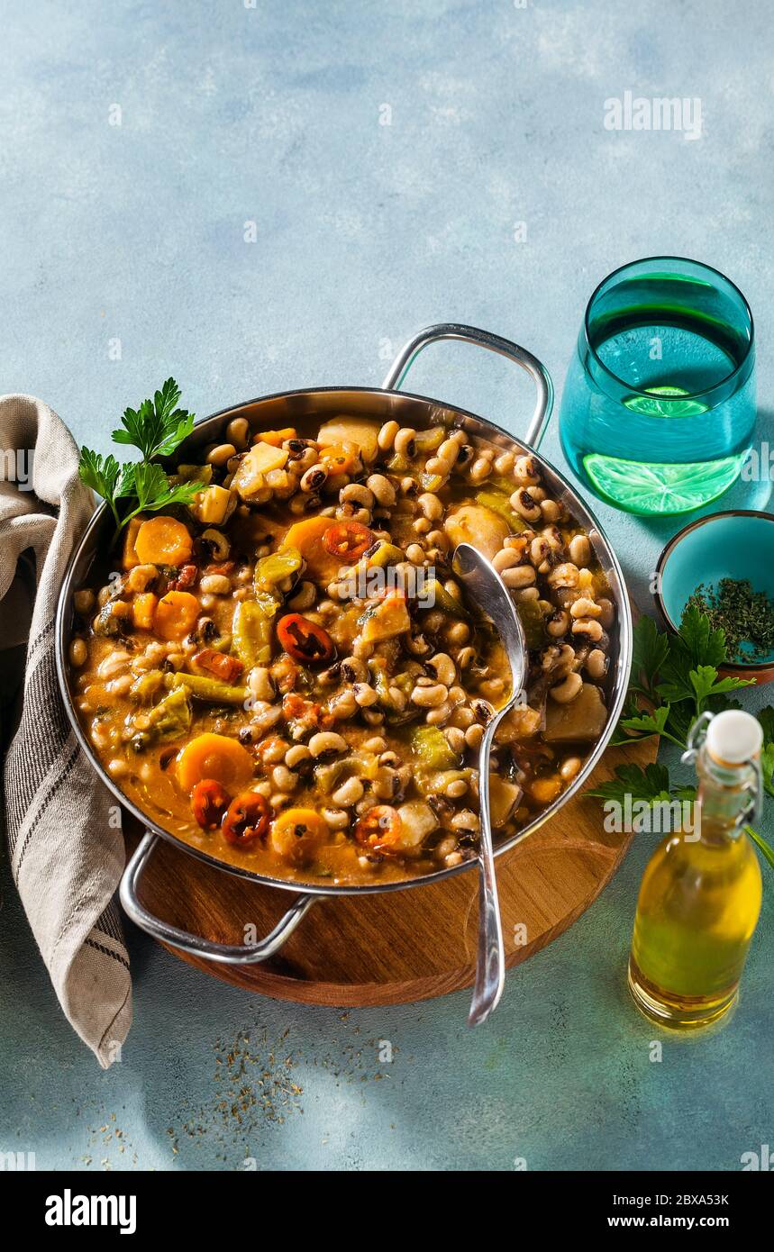 Schwarze Augen Pea Vegan Chili in einer Metallpfanne auf einem Holzständer auf blauem Hintergrund Stockfoto