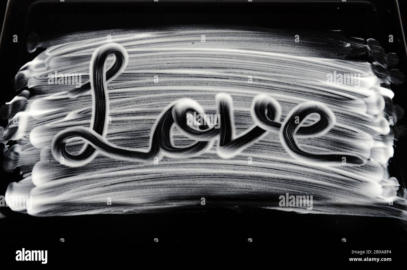 Handgeschriebene Liebesbuchstabierung mit Creme auf schwarzem Hintergrund Stockfoto