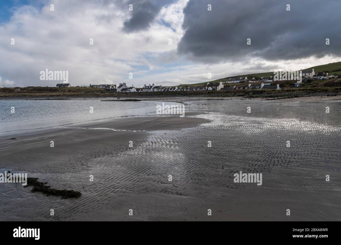 Strand mit Wellen und Algen im Sand und Menschen und Hunde in der Ferne in Port Logan, Dumfries & Galloway, Schottland Stockfoto