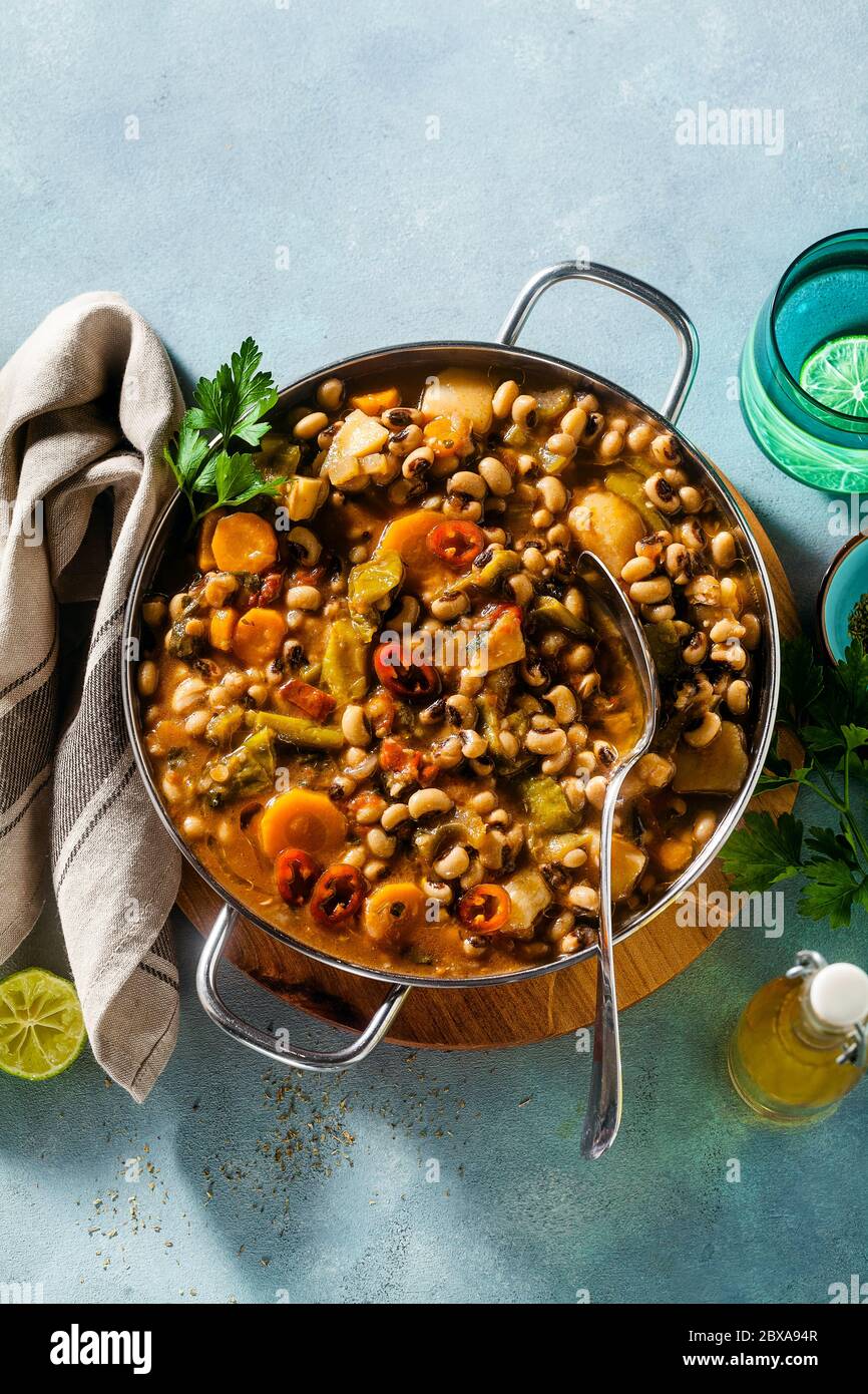 Schwarze Augen Pea Vegan Chili in einer Metallpfanne auf einem Holzständer auf blauem Hintergrund Stockfoto