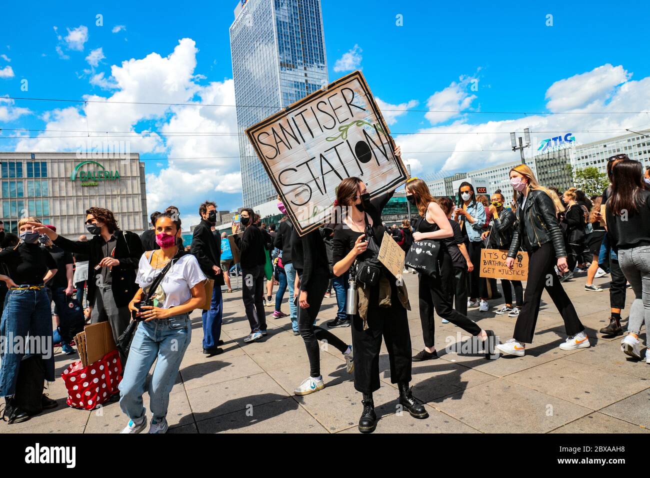 Protestierende mit Gesichtsmaske und Schild "Desinfektionsstation" bietet Handdesinfektionsmittel bei einem Protest von Black Lives Matter auf dem Alexanderplatz Berlin an. Stockfoto