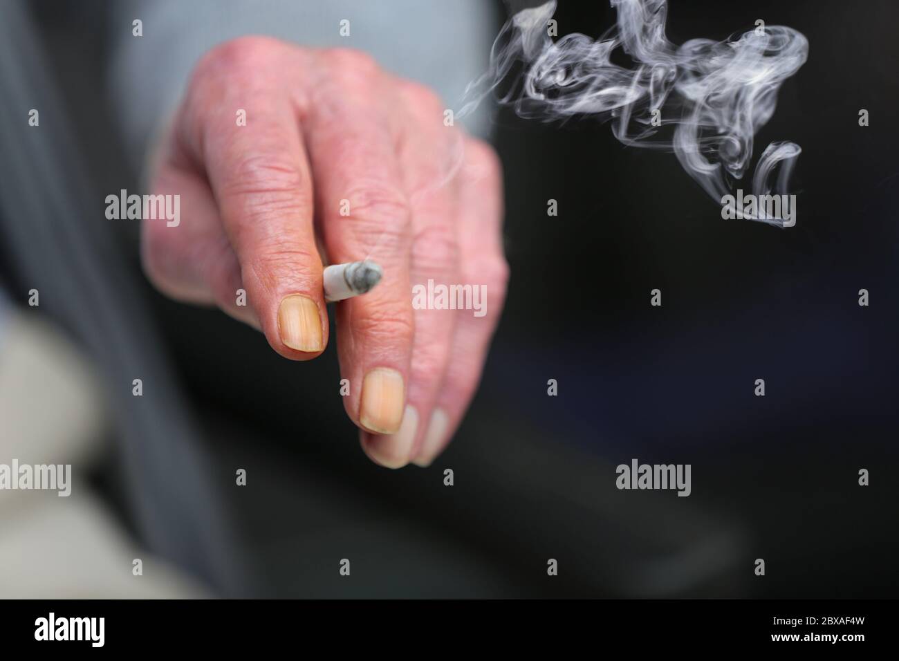 Die Hand einer älteren Person, die eine angezündete Zigarette hält. Die Nägel seiner Finger sind wegen des Teers, Nikotins und Rauchs gelb geworden. Stockfoto