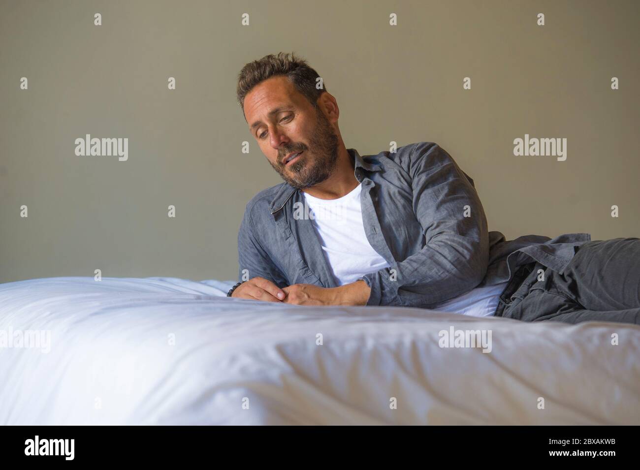 Innenportrait von 30er bis 40er Jahren glücklicher und gutaussehender Mann  zu Hause in lässigem Hemd und Jeans auf dem Bett liegend entspannt zu Hause  nachdenklich und nachdenklich denken Stockfotografie - Alamy