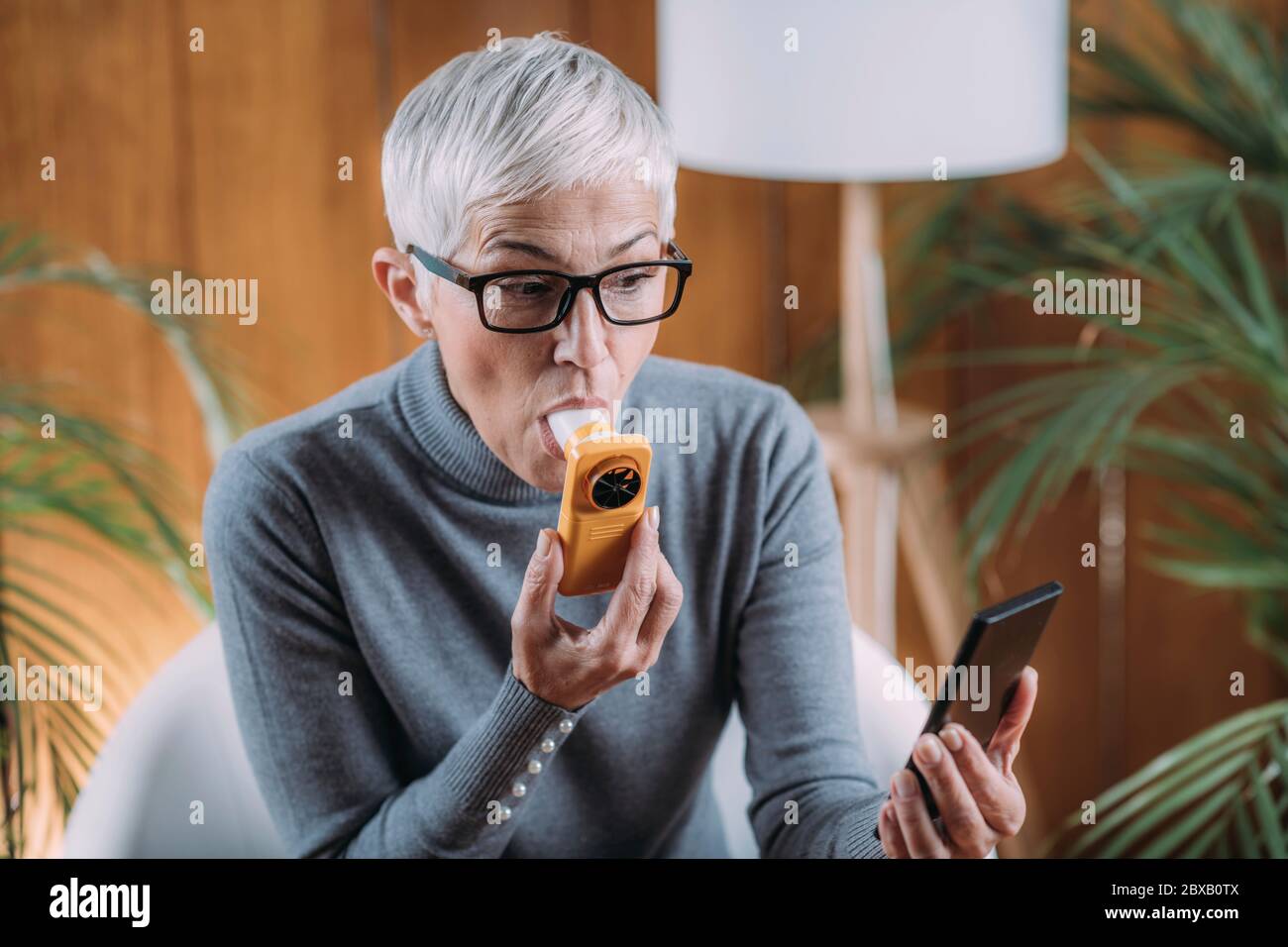 Ältere Frau, die zu Hause Spirometer verwendet Stockfoto