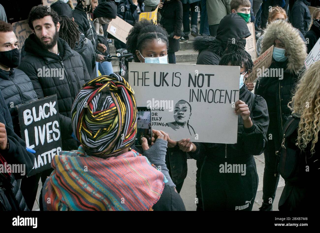 Eine Frau fotografiert zwei junge Mädchen, die ein Plakat halten, das an Belly Mujinga bei dem Anti-Rassismus-Protest im Zentrum Londons erinnert. Stockfoto