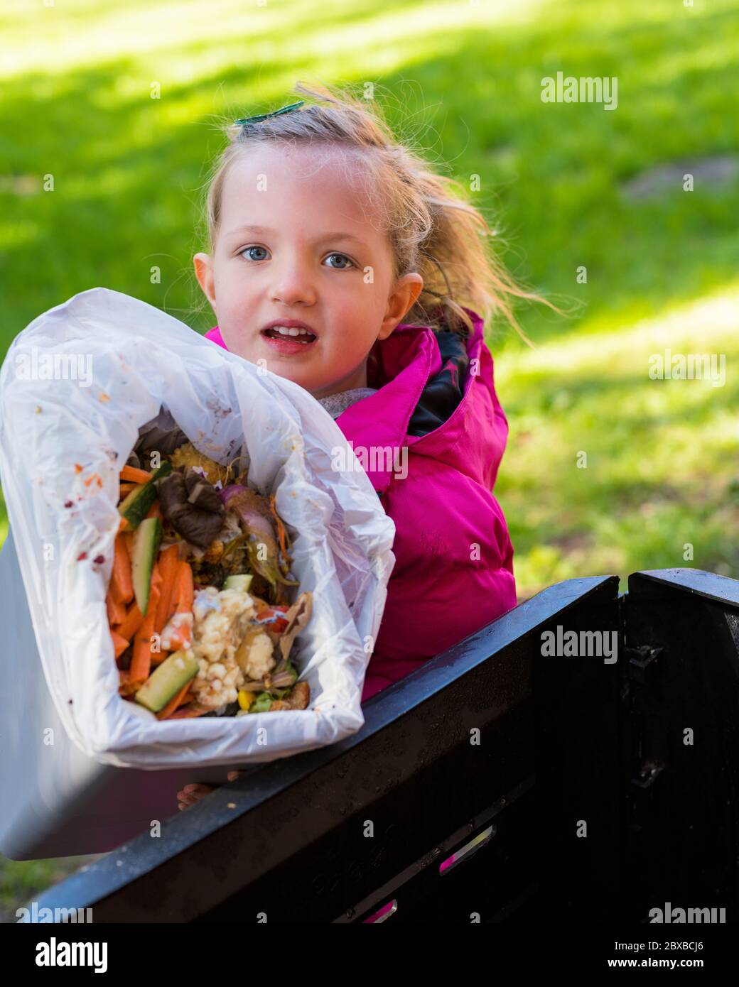 Corona Kompostierung, 4 Jahre altes Mädchen Entleeren der Komposteimer, immer Ihr Kind interessant im Garten. Corona Lockdown Gartenarbeit Stockfoto