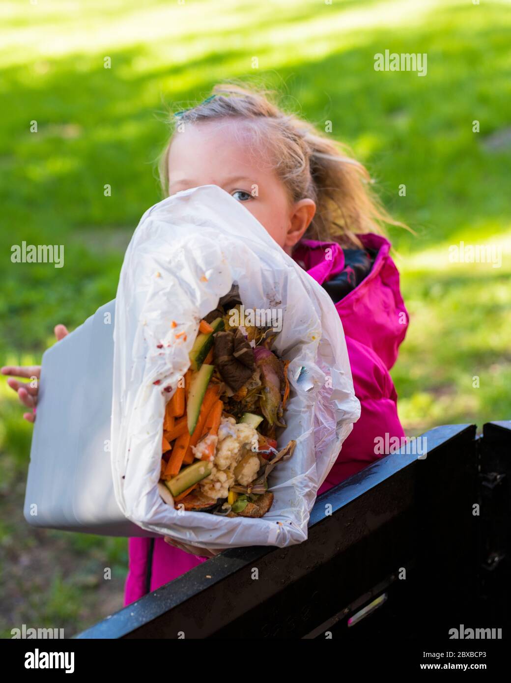 4-jähriges Mädchen, das den Kompostbehälter entleert, Ihr Kind in der Gartenarbeit interessant macht, Vorschulkinder lernen, den Kompostbehälter zu leeren Stockfoto