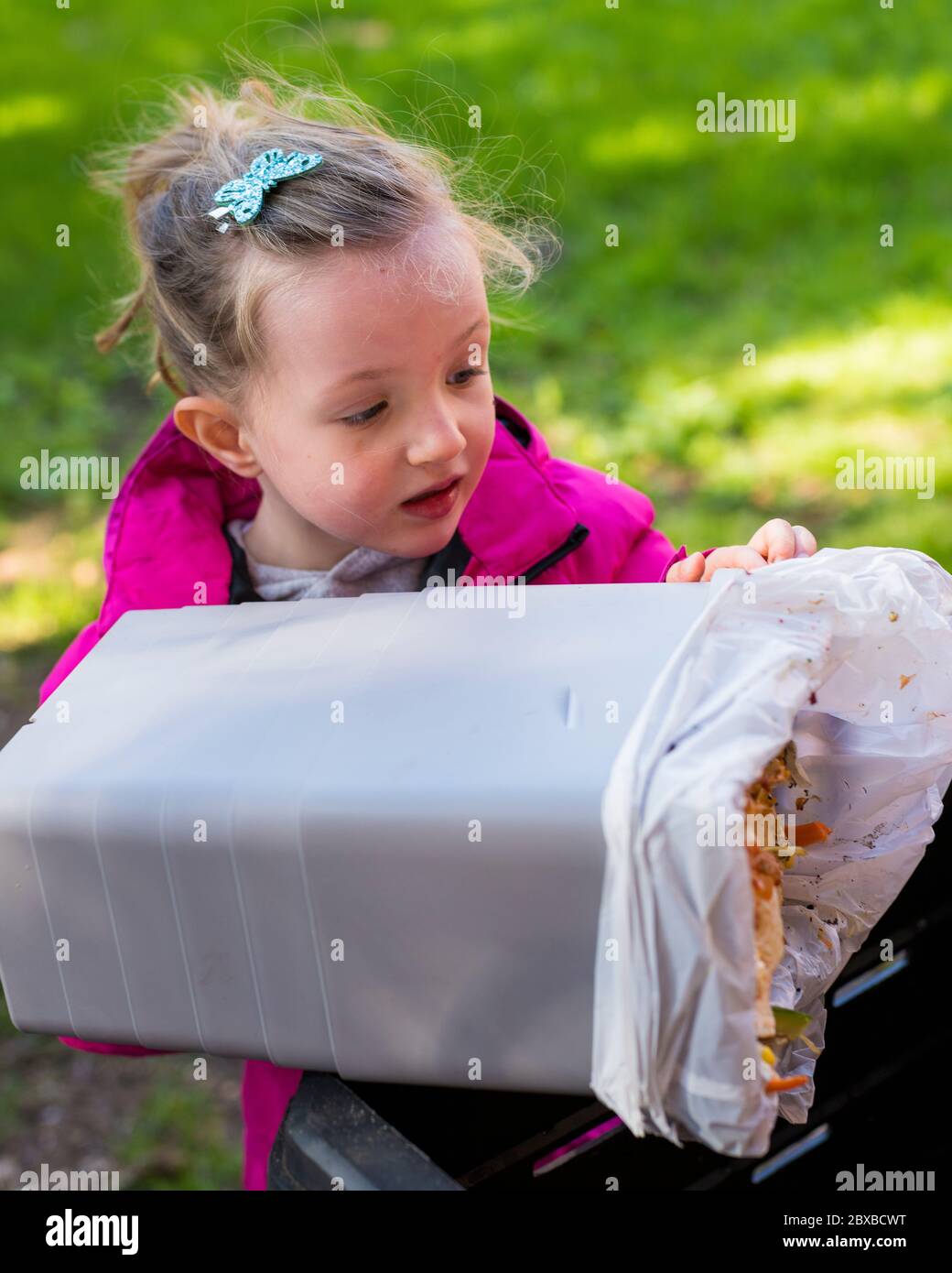 4-jähriges Mädchen, das den Kompostbehälter entleert, Ihr Kind in der Gartenarbeit interessant macht, Vorschulkinder lernen, den Kompostbehälter zu leeren Stockfoto