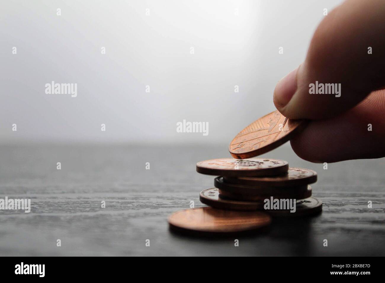Nahaufnahme einer Hand, die einen Penny auf einen Stapel Pennies auf einer schwarzen hölzernen Oberfläche legt. Sparkonzept für die Finanzierung. Stockfoto