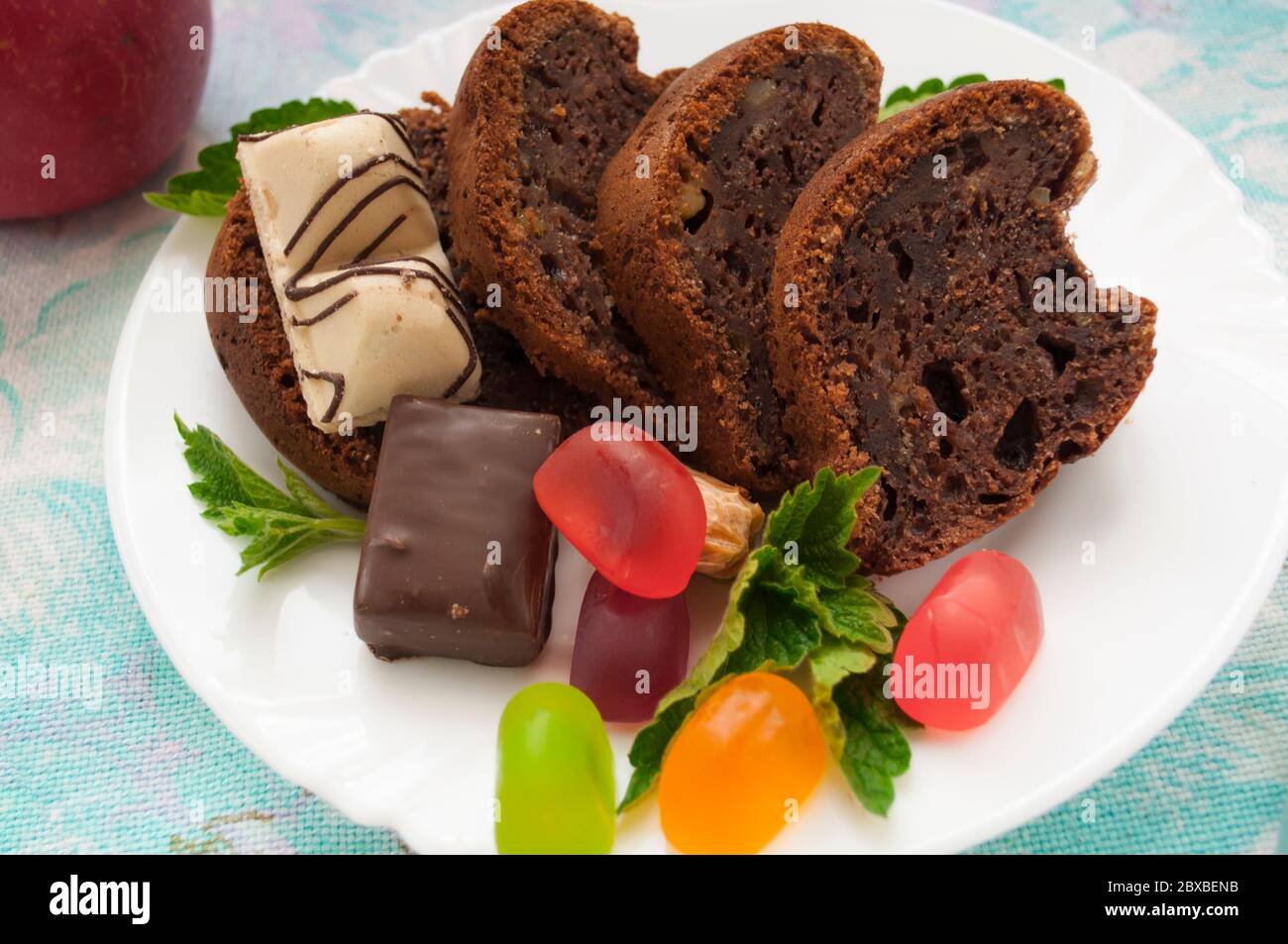 Stücke von Schokoladenkuchen und bunte Gelee Süßigkeiten auf einem weißen Teller mit Minze verziert Nahaufnahme auf einem Hintergrund von farbigen Serviette Stockfoto