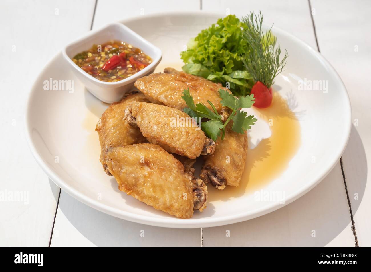 Gebratene Hähnchenflügel mit Fischsauce auf weißem Teller und weißem Holztisch Stockfoto