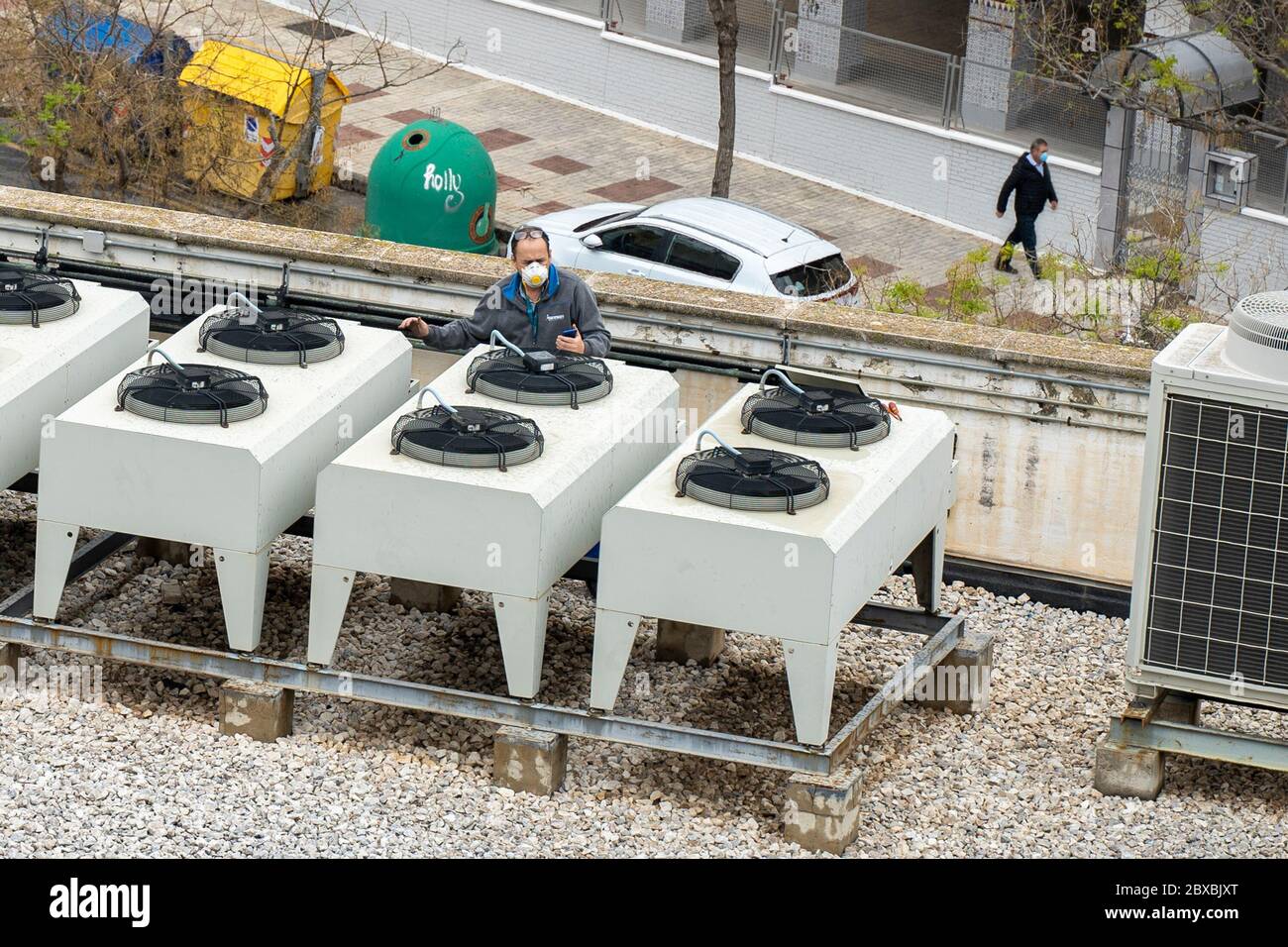 Arbeiter mit Gesichtsmaske und Atemschutzmaske während der COVID-19 Pandemie. Techniker bei der Reparatur der Klimaanlage. Ein alter Mann geht die Straße hinunter und trägt einen medi Stockfoto