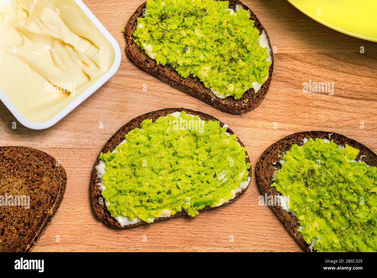 Holzbrett mit Avocado-Sandwiches, Brot und einer offenen Packung Frischkäse. Vegetarisches Gericht. Eine Draufsicht auf ein flaches Layout. Stockfoto