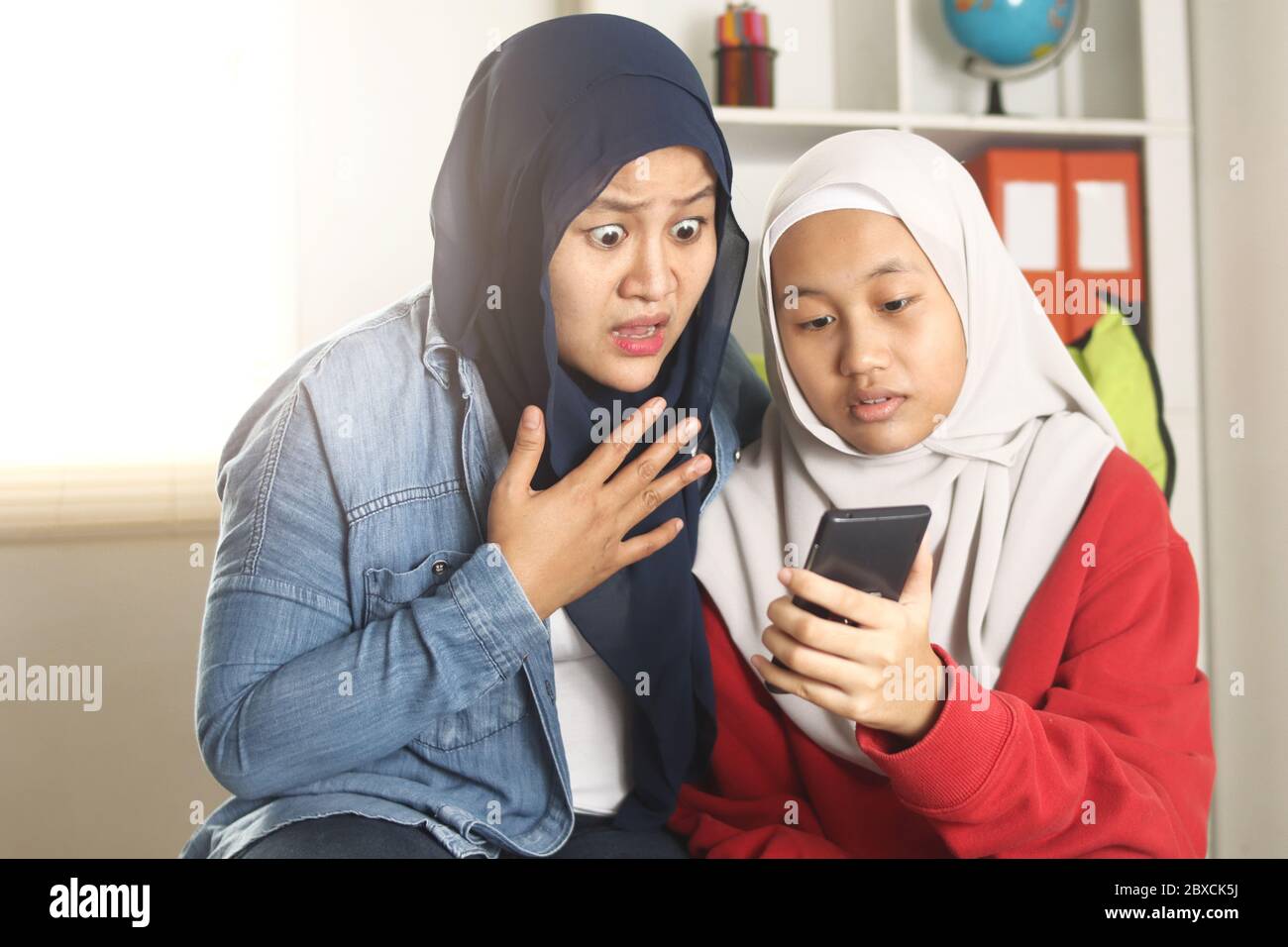 Asiatische muslimische Mutter und Tochter schockiert und besorgt, wenn sie auf ihr Telefon, Surfen im Internet und finden schlechte Nachrichten in sozialen Medien, Casual Lifestyle Stockfoto