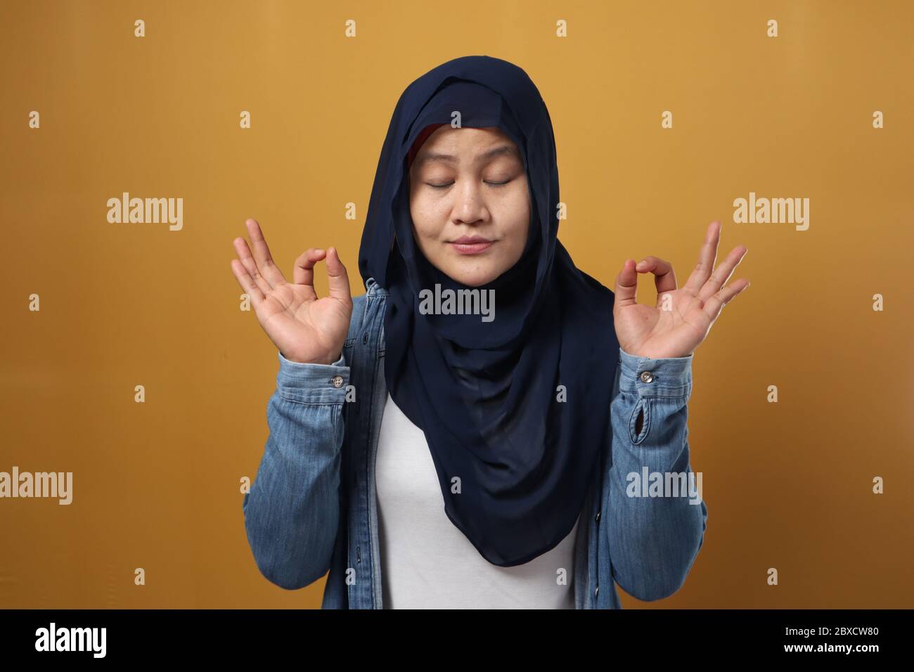 Portrait of Calm entspannt schöne junge asiatische muslimische Frau trägt Hijab in lässiger Stil stehend in Yoga-Pose erhobene Arme, vor gelbem Hintergrund Stockfoto