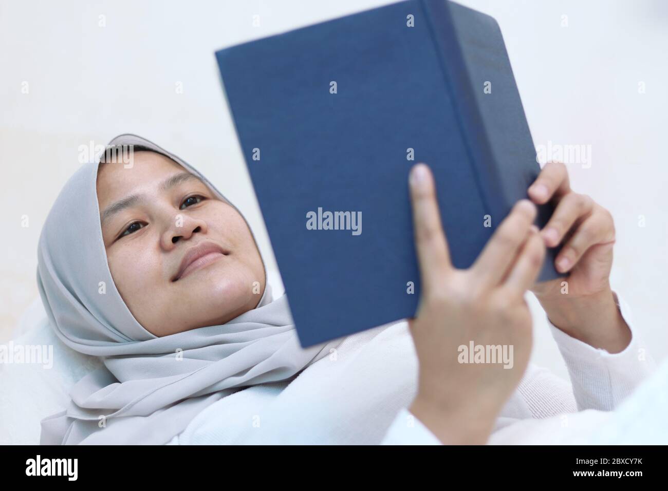 Asiatische muslimische Frau, die den heiligen Koran auf dem Bett liest, um den Koran vor dem Schlaf auswendig zu lernen, islamische Kultur Stockfoto