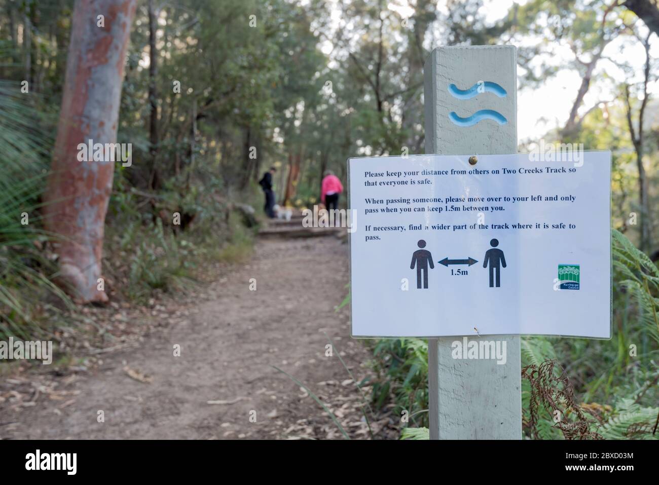 Ein Schild auf einer Buschwanderbahn im nördlichen Vorort Sydney, Australien, warnt Wanderer davor, 1.5 Meter voneinander entfernt zu bleiben, mit verschwommenen Menschen im Hintergrund Stockfoto