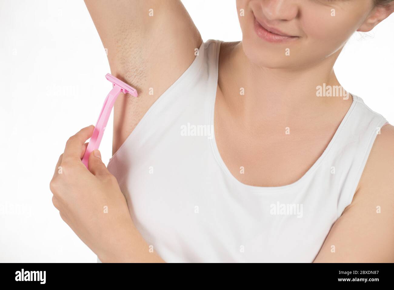 Schöne junge Frau in einem weißen T-Shirt lächelt und tut eine Enthaarung von Achselhöhlen oder Rasieren Achselhöhlen rosa Rasierer auf einem weißen Hintergrund Stockfoto