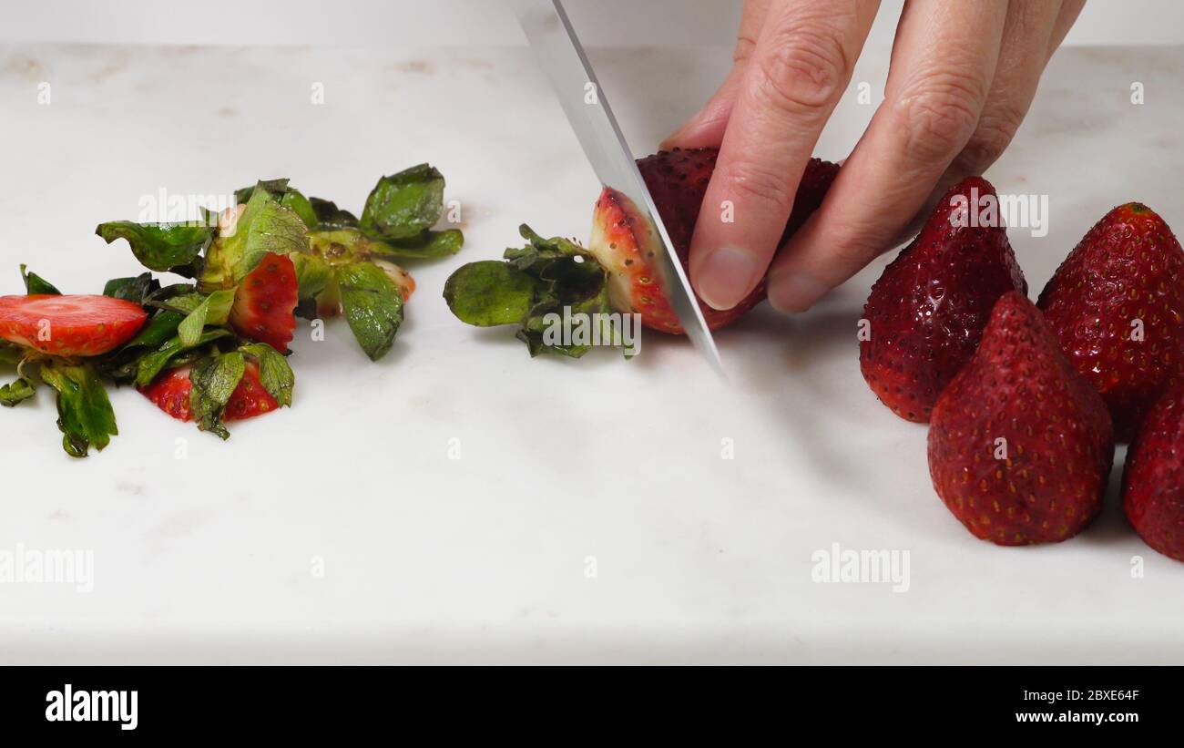 Frau schneidet frische reife Erdbeeren zum Dessert, Nahaufnahme auf weißem Hintergrund Stockfoto
