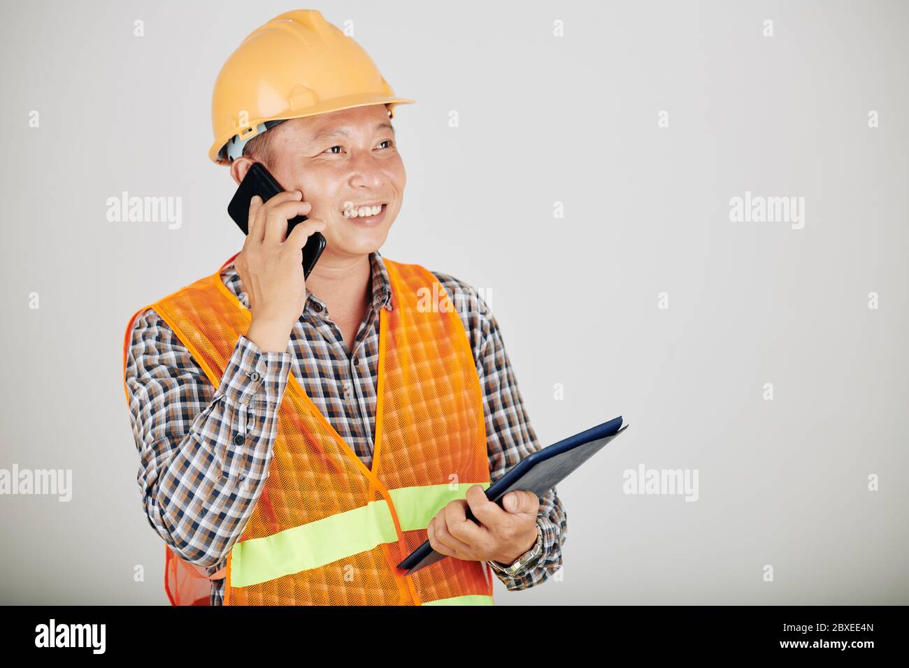 Lächelnder Auftragnehmer mit digitalem Tablet, der mit dem Kunden telefoniert Stockfoto