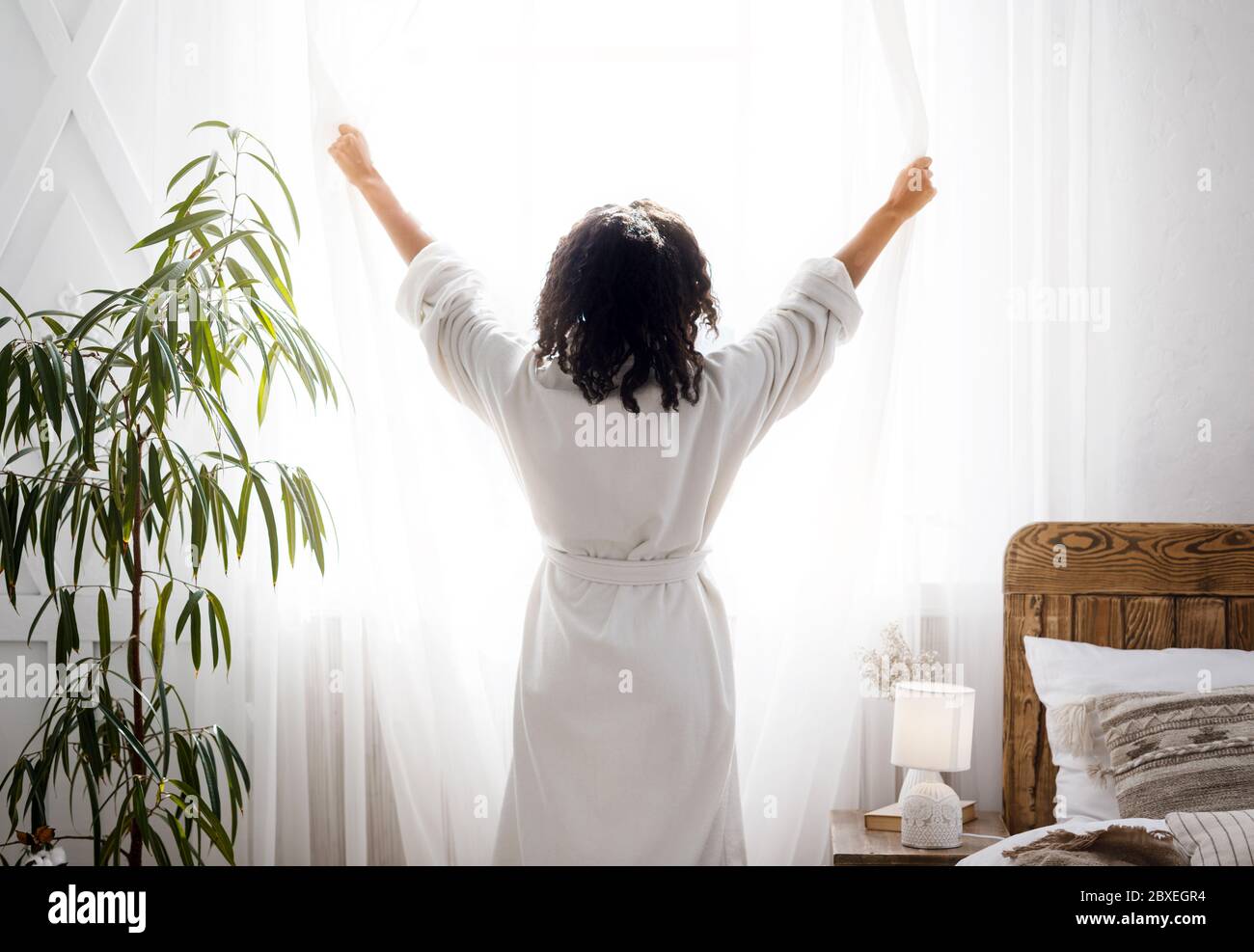 Perfekter Morgen. Unerkennbare Frau in weißen Bademantel öffnen Fenster Vorhänge zu Hause Stockfoto