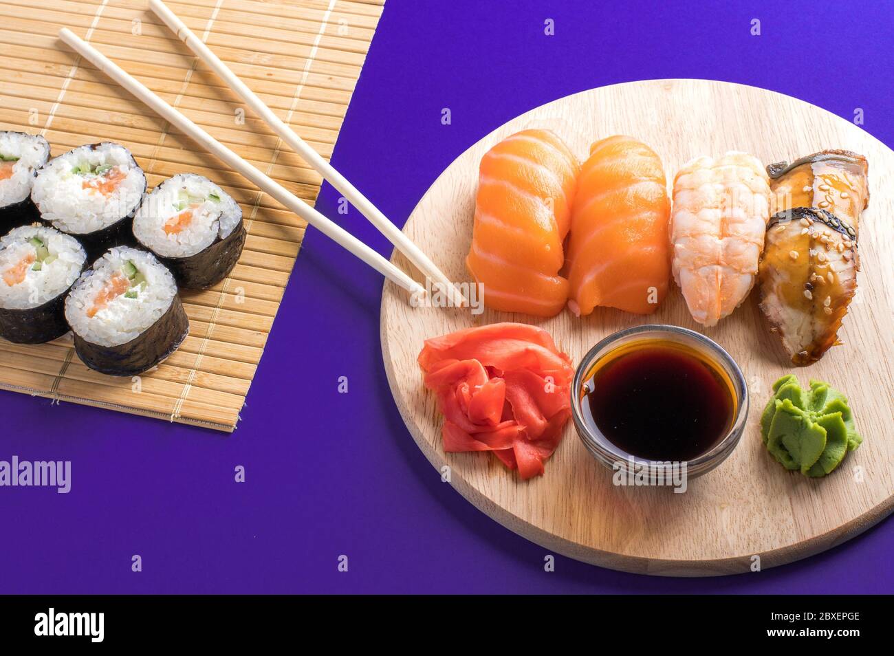 Nahaufnahme von frischem Sushi und Brötchen auf Holzbrett und Bambusmatte. Violetter Hintergrund Stockfoto