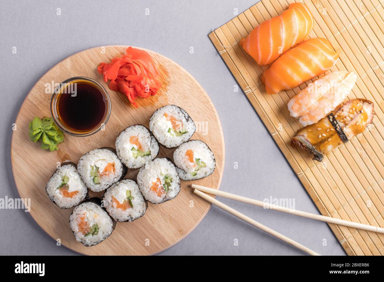 Sushi-Set auf Bambusmatte und Holzbrett. Sushi-Brötchen, Wasabi und Ingwer auf grauem Hintergrund Stockfoto