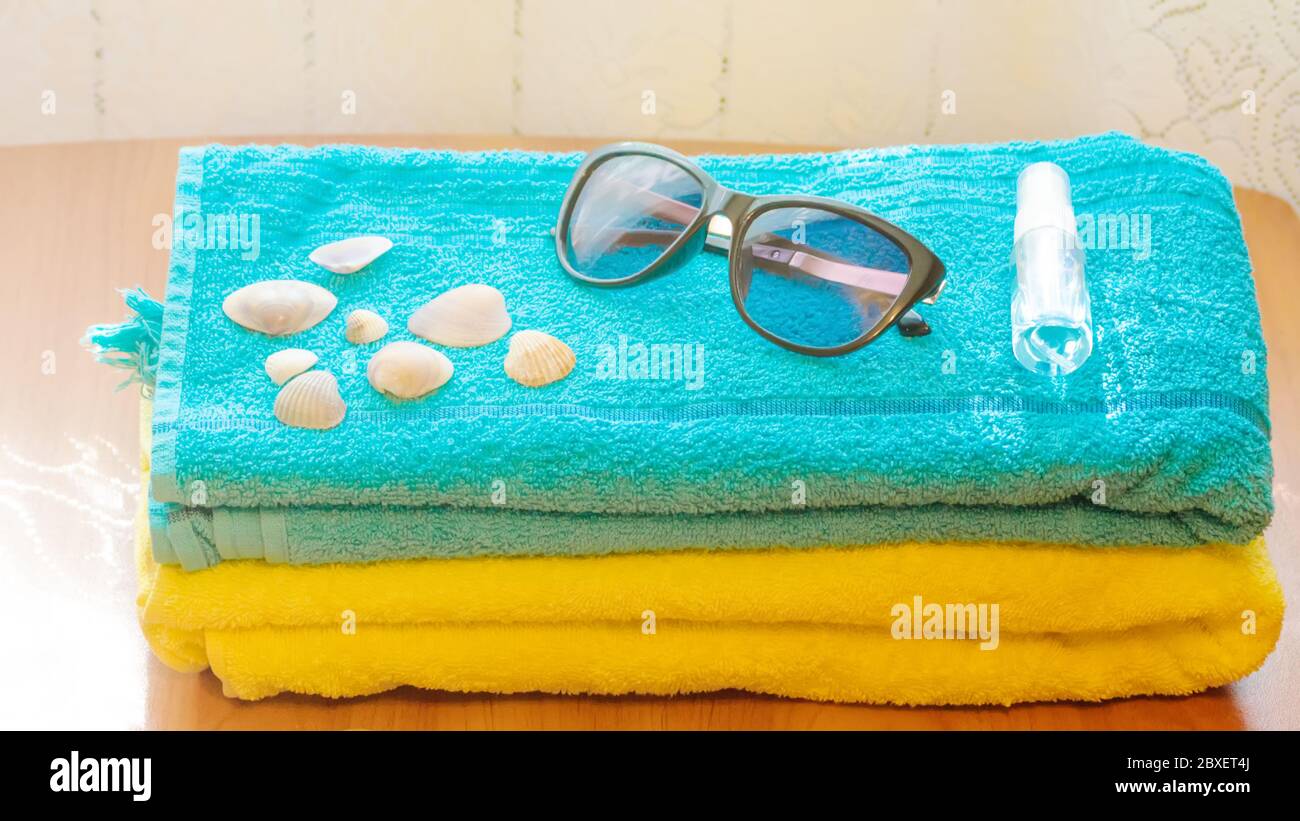 Desinfektionsflasche, Sonnenbrille und Muscheln liegen auf einem blauen Handtuch. Das Konzept eines Sommerurlaubs in einer neuen Realität. Stockfoto