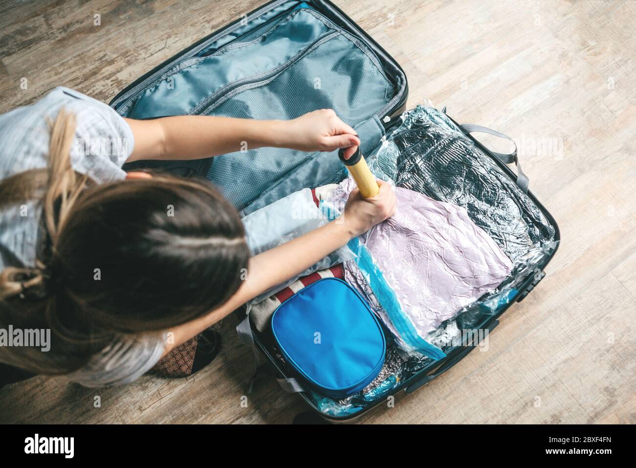 Ein Mädchen packt Dinge oder Kleidung mit einer Vakuumpumpe, um Platz in einem Reisekoffer zu sparen. Stockfoto