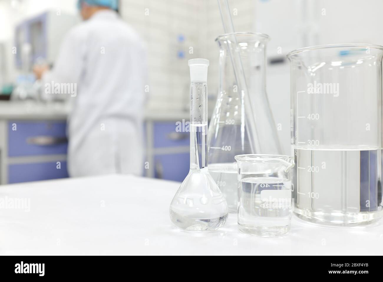 Blur-Wissenschaftler, der in einem Chemistry Science-Labor mit Kolben, Becher und Glaswaren arbeitet, die klare flüssige Chemikalien enthalten. Stockfoto