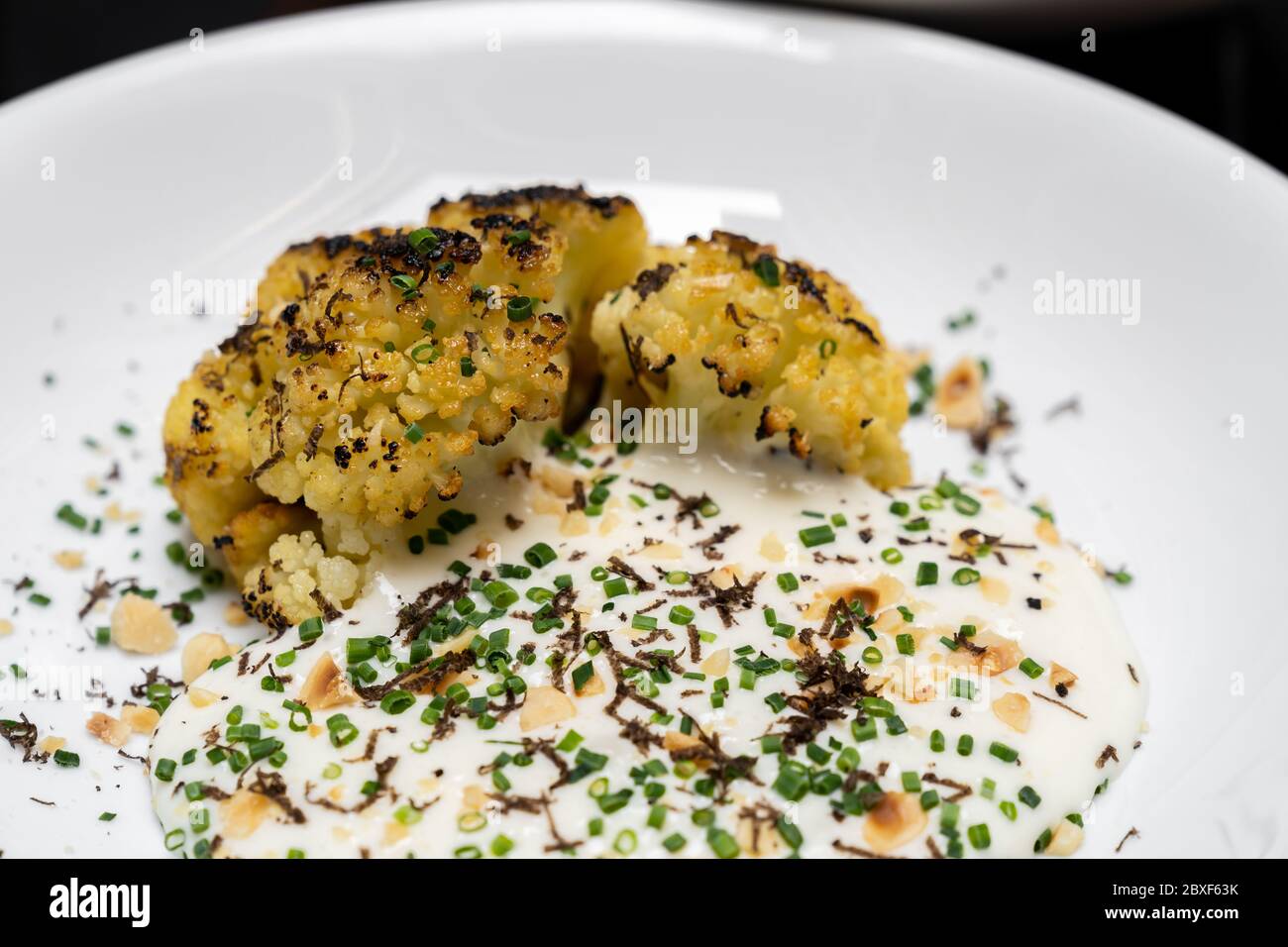 Geröstete Blumenkohl mit Parmesan und Haselnuss Belag mit Frühlingszwiebeln und Blumenkohlensuppe, Gourmet-Rezept der internationalen Küche. Restaurant Gastro Stockfoto