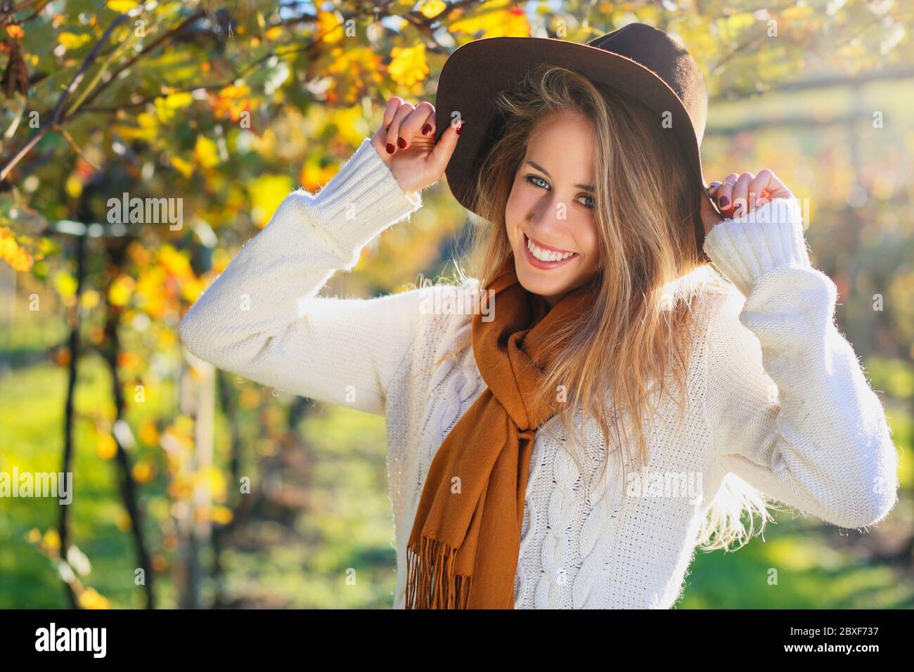 Lächelnde Frau mit elegantem Hut genießen Herbstsonne auf dem Land Stockfoto