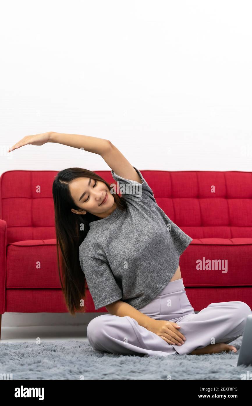 Asiatische Frau mit Laptop für Online-Coaching zu tun, während die Ausübung im Lotus-Position sitzen. Aktive junge Frau tun Dehnung Übung im Leben Stockfoto