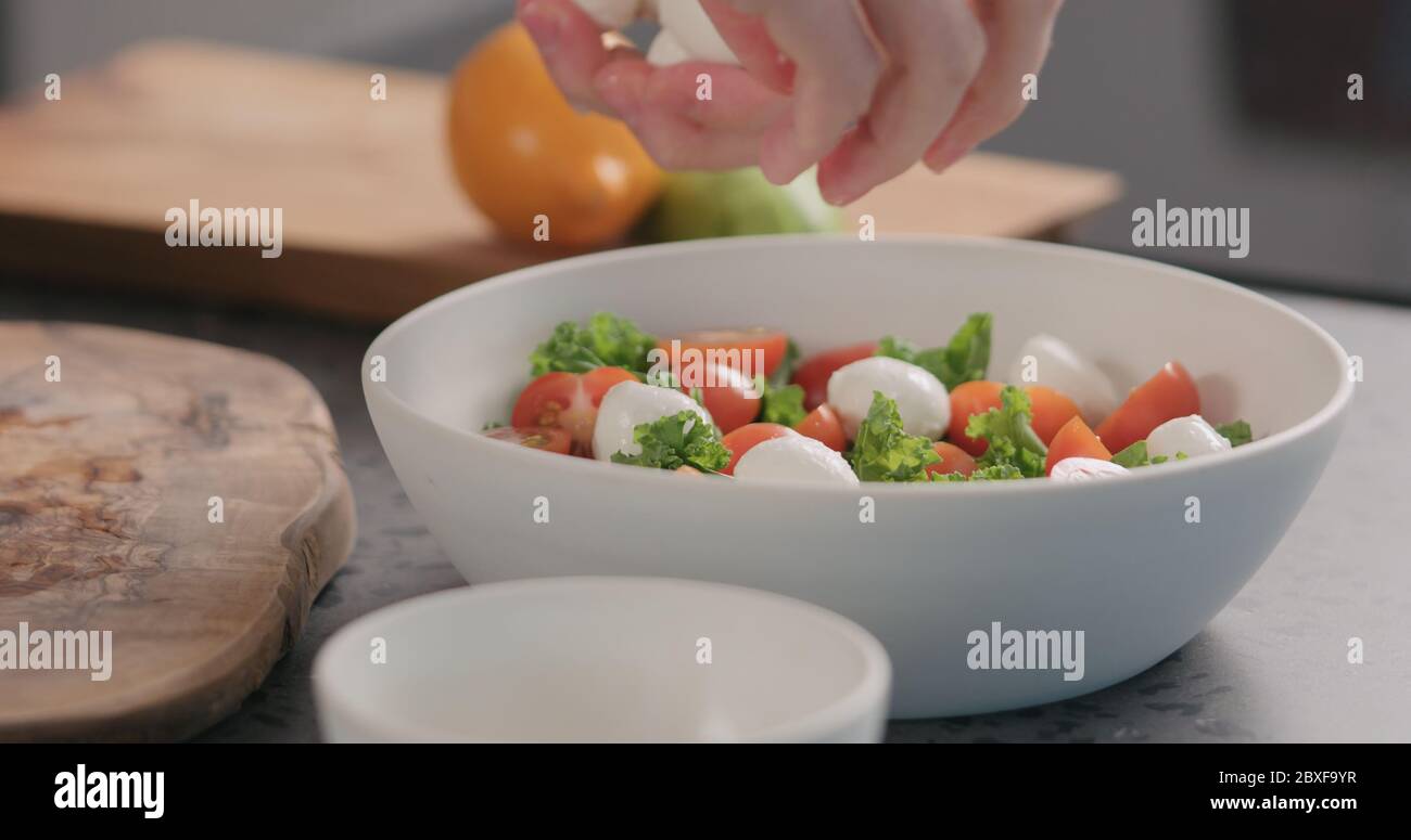 Man fügt Mozzarella in Salat mit Grünkohl und Tomaten in Weiße Schüssel auf Küchenarbeitspe Stockfoto