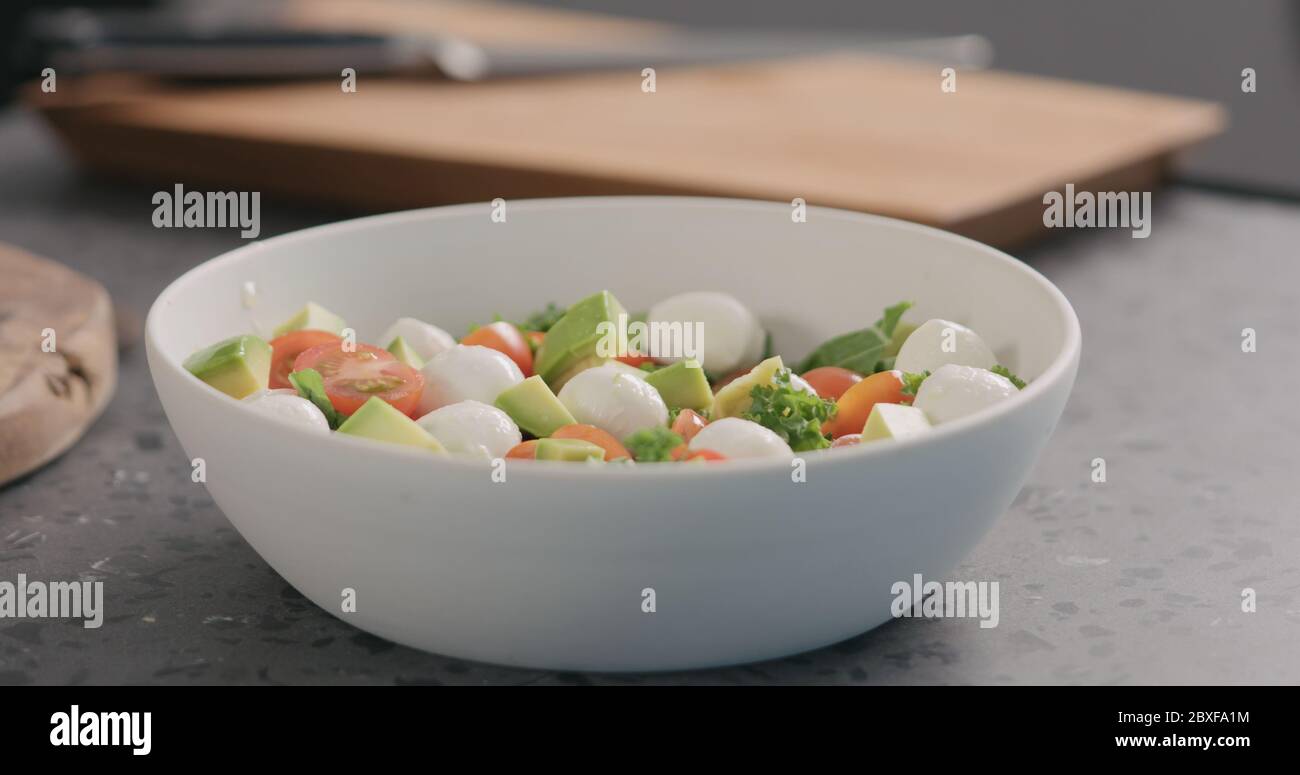 Orangenzitrone in Salat mit Grünkohl, Avocado, Mozzarella und Tomaten in einer weißen Schüssel auf der Küchenarbeitsfläche geben Stockfoto